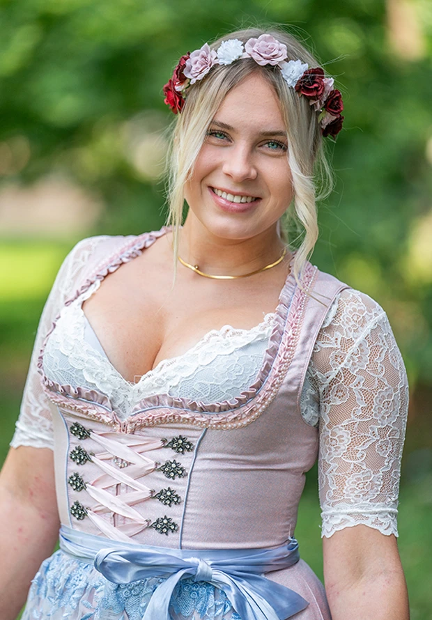 Eine junge Frau lächelt, trägt ein traditionelles Dirndl und einen Blumenkranz.
