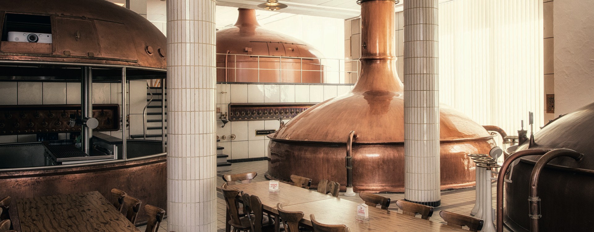 Innenansicht einer Brauerei mit großen Kupferkesseln und einem Holztisch.