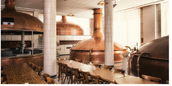 Ein Raum mit großen Kupferbraukesseln und Holztischen dient als Brauerei.