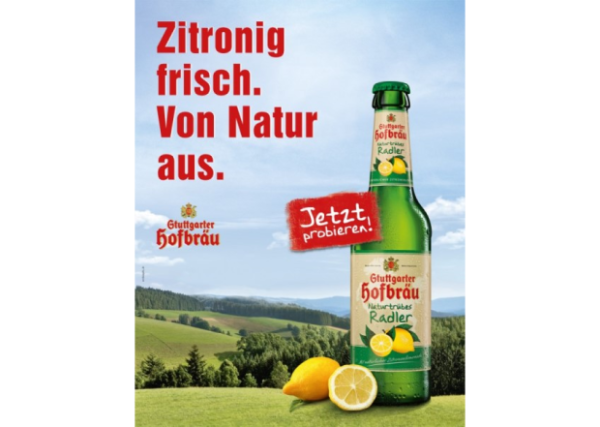 Eine grüne Flasche steht neben zwei Zitronenhälften vor einer Hügellandschaft.