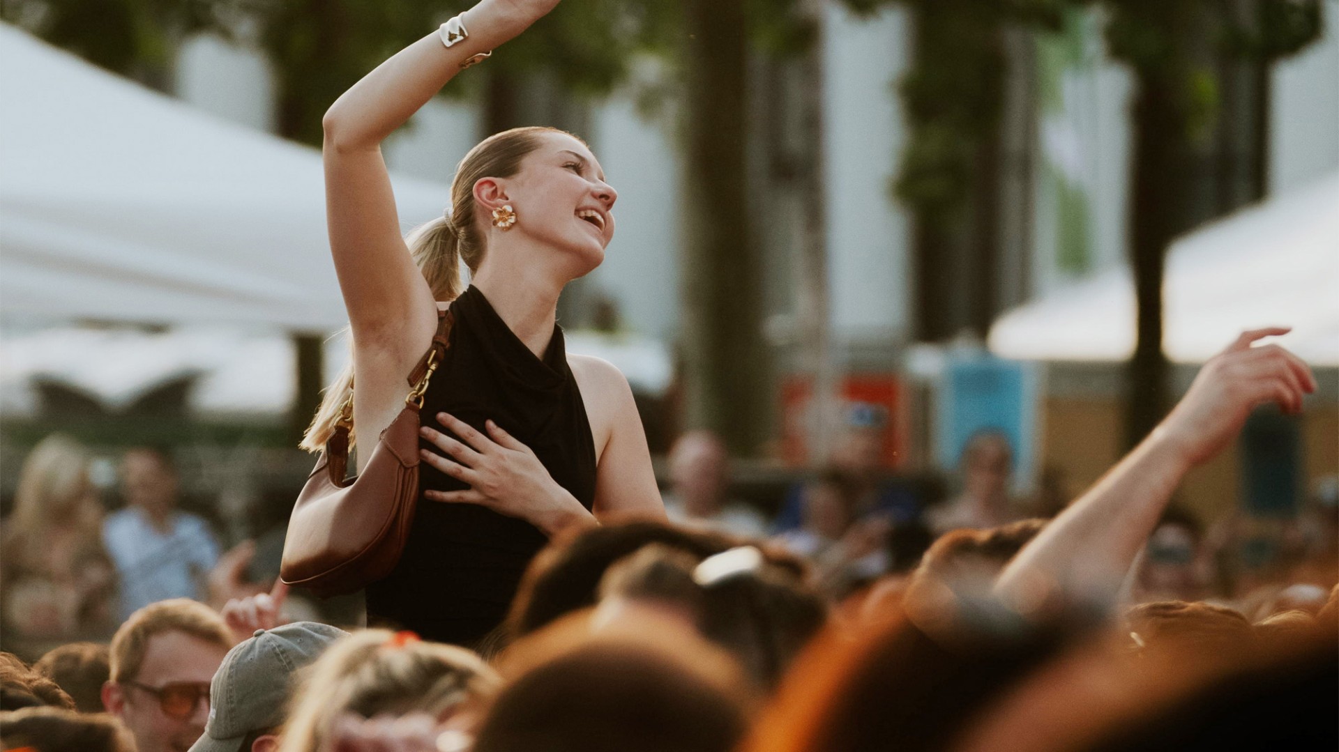 Menschenmenge bei einem Open-Air-Event. Eine Frau hebt die Hand und lächelt.