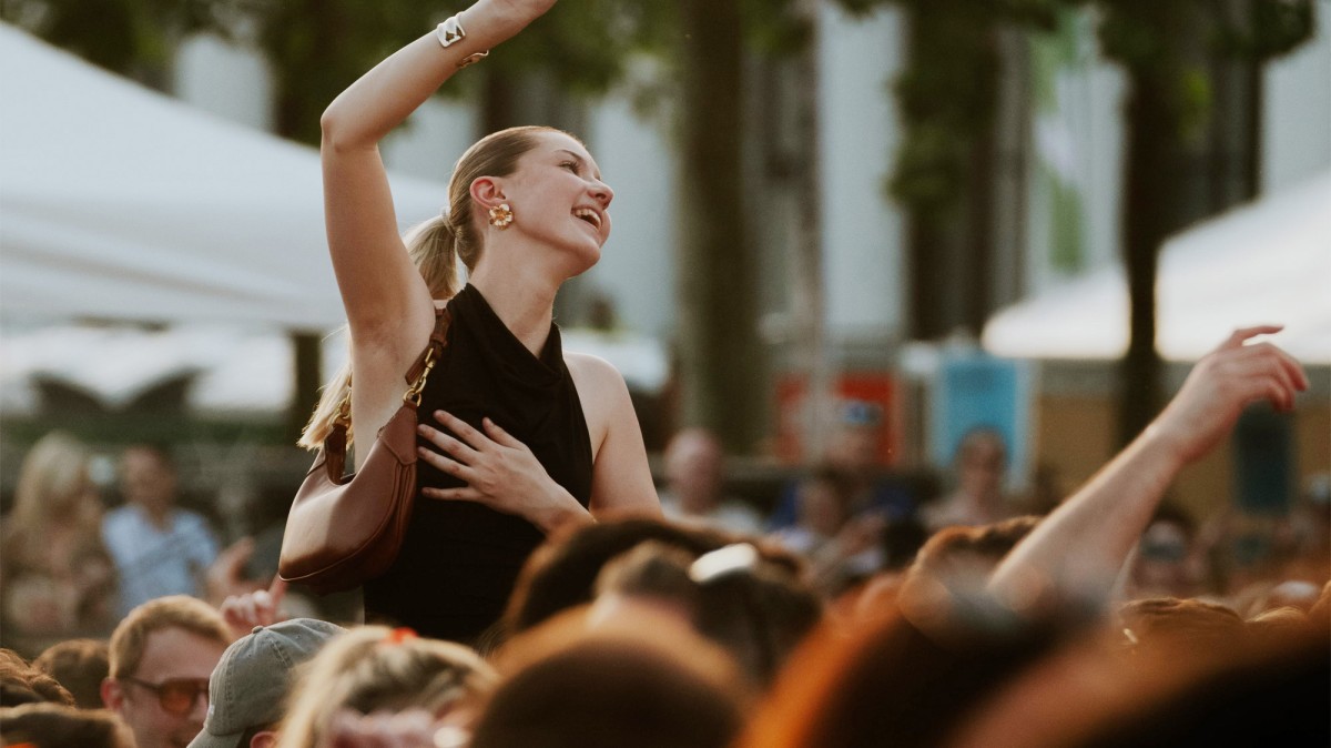 Menschenmenge bei einem Open-Air-Event. Eine Frau hebt die Hand und lächelt.