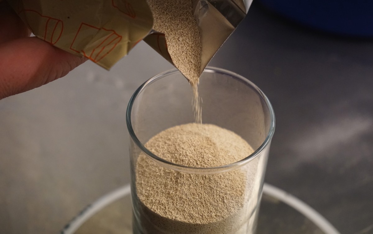 Eine Hand schüttet feines, helles Pulver aus einem Beutel in ein Glas.