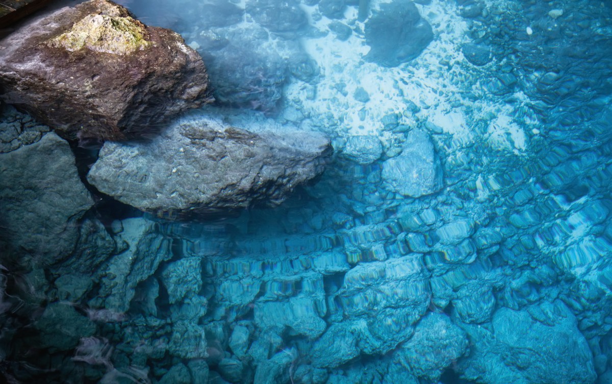 Ein klareblaues Gewässer mit großen, eingetauchten Steinen ist sichtbar.