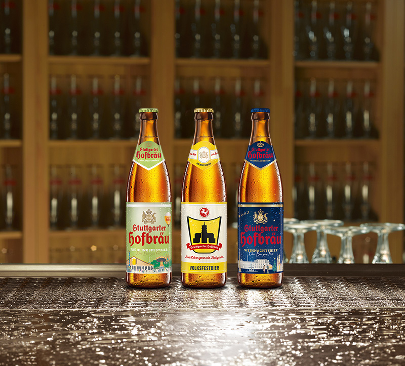 Drei Bierflaschen stehen auf einer nassen Oberfläche vor einem Regal voller Flaschen.