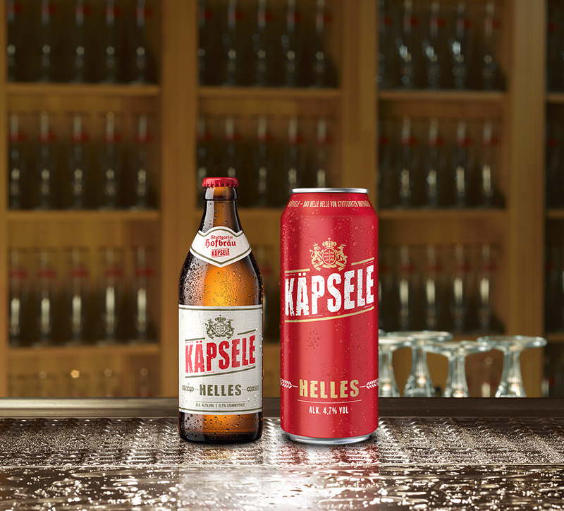 Eine Käpsele Bierflasche und eine Dose stehen auf einer nassen Oberfläche mit vielen leeren Gläsern im Hintergrund.