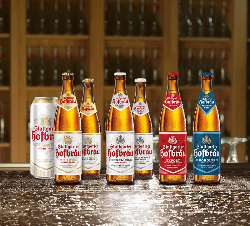 Sechs verschiedene Bierflaschen und eine Dose stehen auf einer nassen Oberfläche, im Hintergrund ein Regal mit Flaschen.