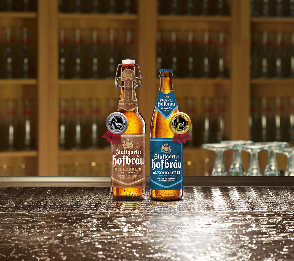 Zwei Bierflaschen stehen auf einem nassen Holztisch vor einem Regal mit Flaschen.