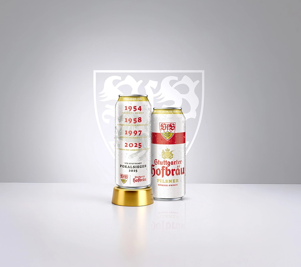 Zwei Dosen Stuttgarter Hofbräu mit VfB-Stuttgart-Design stehen nebeneinander. Im Hintergrund ist ein weißes Wappen zu sehen.