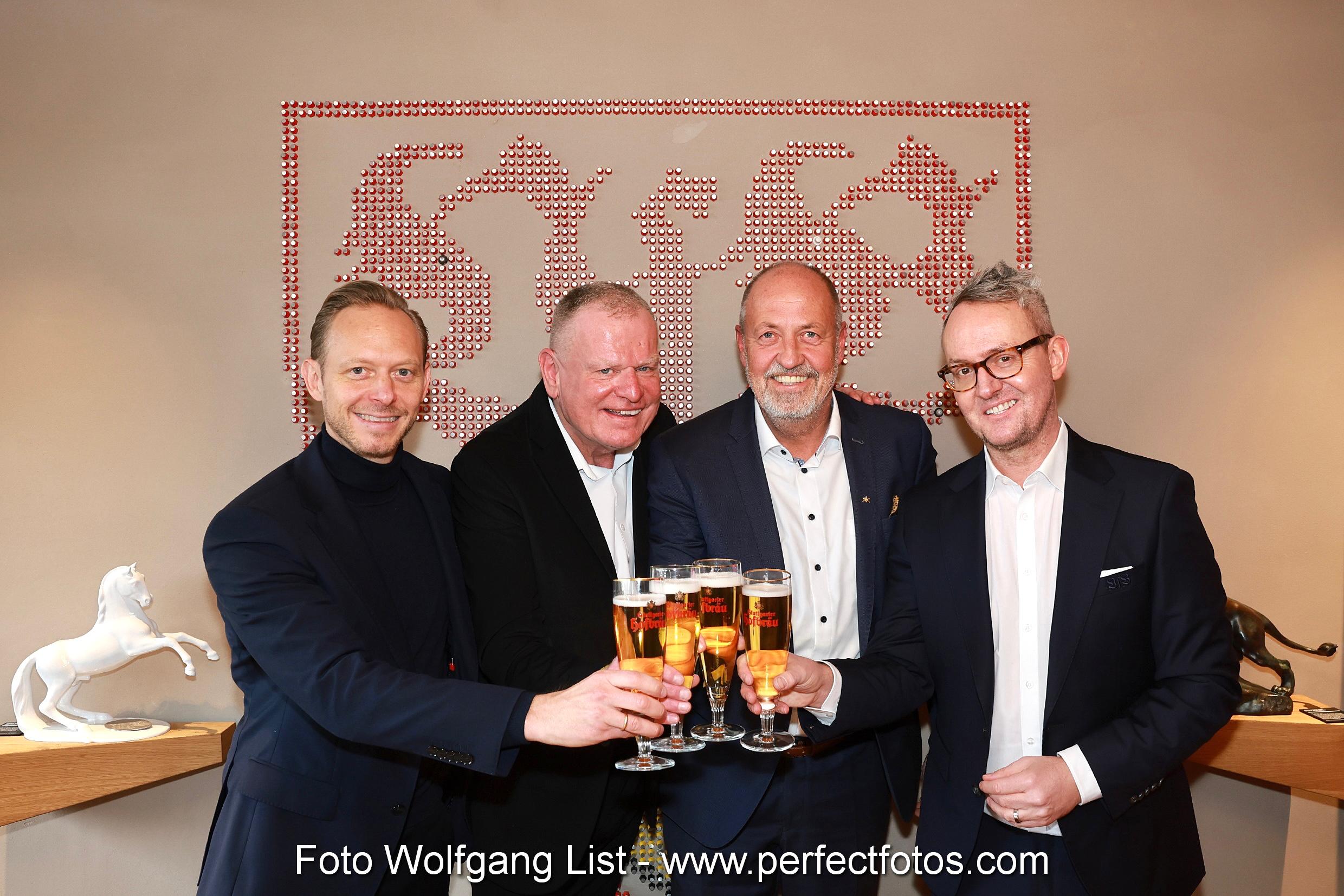 Vier Personen stehen vor dem VFB Logo und stoßen mit 4 Biergläsern an.