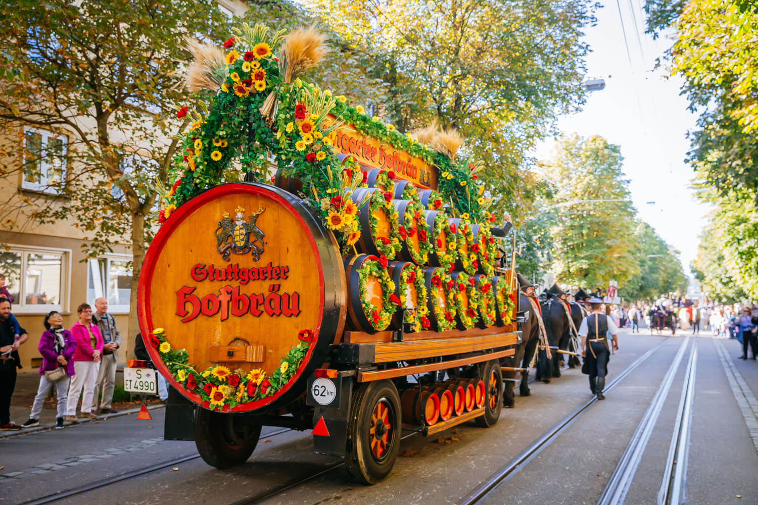 Ein mit Blumen und Fässern geschmückter Festwagen wird von Pferden gezogen.